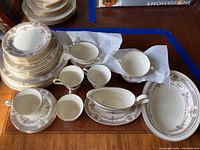 Wide view of stacked plates in varying sizes, teacups and saucers, gravy boat and oval serving platter all with Persian Rose pattern by Minton.