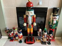 Nine wooden nutcracker figures of varying sizes arranged in front of fireplace, showing overall size range and variety