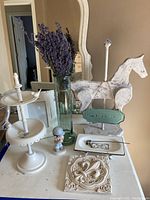 Full lot display on table showing all items including glass vase with lavender, wooden carousel horse, jewelry display stand, Precious Moments figurine, metal tin sign, decorative tile, and French dish.