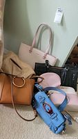 Grouping of six assorted ladies handbags on floor in various colors and styles