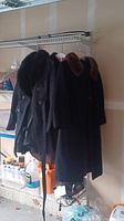 Two women's coats hanging on a rack in a garage/storage area; one with a faux fur collar and one is cashmere.