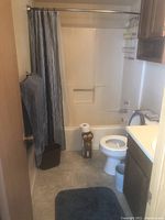 Bathroom overview showing shower curtain, towels hanging on wall, wastebasket on floor, bath rug on floor, and toilet.