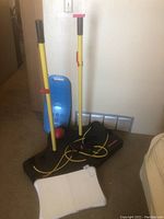 Exercise machine with yellow vertical poles, resistance bands, and a red ball, alongside the white Wii Fit balance board on carpet.