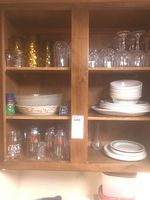 Kitchen cabinet shelves containing amber textured glasses, clear cut glasses, stemware, printed drinking glasses, and Corelle dishes neatly stacked.