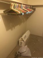 Closet rack with over 60 multi-color plastic hangers hanging. Cardboard box and plastic bag storage below.