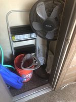 Holmes black pedestal fan beside a metal step stool and orange bucket inside closet