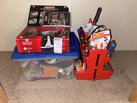 Photo showing the clear plastic bin containing assorted hardware and supplies with the red tool organizer and Craftsman drill box on top.