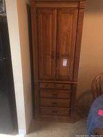 Tall oak cabinet with closed two doors on upper section and four drawers below, photographed from front