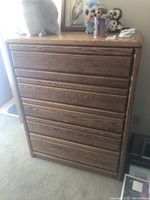 Front view of the oak chest of drawers showing all five drawers closed, placed on carpeted floor, with some small stuffed animals and decor items on top.