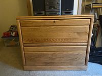 Full frontal image of the oak lateral file cabinet showing its two drawers, flat top surface, and locking mechanism.