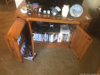 Front view of oak media cabinet with double doors open showing shelves with media components and DVD storage.