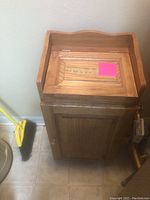 Oak trash box with hinged lid, decorative inlay on top panel, standing on kitchen floor near wall.