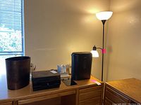 Black floor lamp, Ativa paper shredder, electric calculator, paper cutter, all placed on a wooden surface in a lit room near window.