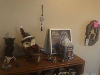 Overview of owl figurines, note board, tissue box, and small bird figurines on wooden shelf against beige wall.