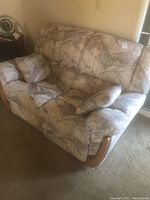 Angle view of the recliner loveseat showing fabric pattern, wooden armrest detail, and one cushion on the seat.