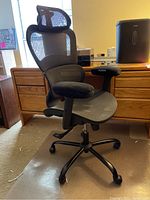 Front angled view of black mesh Rottnen office chair placed on a protective floor mat near wooden furniture, showing headrest, seat, and armrests.