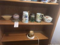 Photo showing Royal Worcester mugs and covered dish on wooden shelves along with a green glass candle holder and a small beige bowl