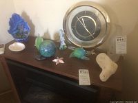 Full view of seashore collectibles on wooden cabinet including clock, glass coral, dolphin figurine, starfish, and coral decor.