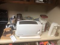 Overview photo showing KitchenAid toaster, popcorn popper, stoneware jars and bowls, manual can opener and electric can opener on kitchen countertop.