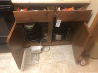 Photo of open cabinet showing vintage Pyrex baking dish with floral pattern, glass lid, crockpot, and other cookware stored inside