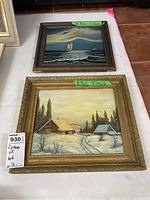 Framed oil paintings of sailboat and snowy cabin scene with seller's tag and artist's name labels visible.
