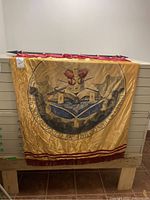 Full view of religious banner with emblem and text laid out flat and hanging from wood rod with loops