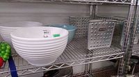 Three Primagera ceramic bowls and a metal wire basket displayed on metal shelves.