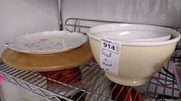 Two beige ceramic bowls next to a white floral serving plate placed on a wooden lazy Susan.