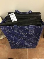 Vertical stack of six black rectangular contact print frames inside a blue floral-patterned fabric bag, showing the top and sides of frames.