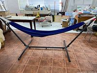 Full view of hammock suspended on a black metal stand indoors on tiled floor.