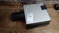 Silver Artograph designer projector with black lens on a tiled floor, shown from left side angle.