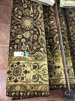 Rolled-up view of the brownish-maroon floral rug with green and beige floral patterns and border design visible, showing detailed weave and pattern.