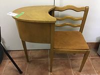 Side view showing the wooden semi-circular telephone table attached to the chair with three wavy back slats and upholstered brown seat.
