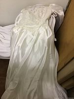 Full-length view of the vintage wedding dress laid out showing lace bodice and satin skirt with some stains.