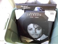 Two black and white wood prints of Michael Jackson stacked in a green bin, showing front faces with signs of wear and protective white corner guards.