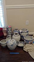 Wide shot showing all 9 blue and white ceramic items including jars, planters, garden stool and vase arranged on floor.