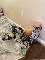Wide view of assortment of black wrought iron candle holders and clear glass candle plates scattered on floor near wall.