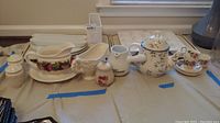Wide view of all 22 ceramic serving pieces including teapots, shakers, pitchers, platters, and small dishes laid out on table.