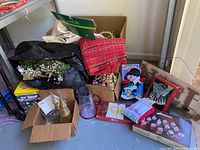 Wide view of assorted Christmas decorations and linens in boxes and bags showing wreaths, lights, figurines, and linens.