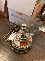 Photo showing two large ornate decorative keys, a small urn-shaped vase with handle, and three decorative plates stacked below along with a clear ribbed glass vase.