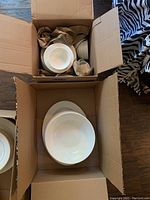 Box with various white plates and bowls stacked, showing the basket weave pattern on some edges.