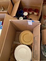 Overview of two boxes showing eight mugs in multiple colors and fifteen plates including yellow and white ceramic plates.