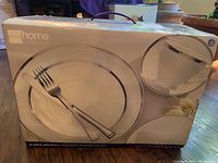 Box front image showing Colin Cowie home collection dinnerware set with image of plate and cup with silver rim.