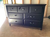 Front view of espresso finished double dresser showing seven drawers with different silver toned knobs and handles, marks visible on drawer fronts.