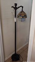 Full view of the lamp showing metal stand, base, and stained glass shade with floral pattern, lamp off.