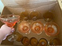 Amber-tinted wine glasses and pink margarita glasses in a cardboard box, hand holding a pink margarita glass.