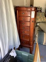 Front view of tall cherry wood jewelry chest with seven drawers and side cabinet doors.
