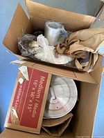 Photo showing the cardboard box with large aluminum pot visible inside along with some fabric aprons or oven mitts