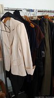 Clothing rack showing cream Worthington blazer, dark tees and pants hanging on wooden and plastic hangers.