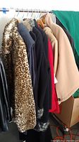Photo showing 9 different ladies coats on hangers in various colors and materials including faux fur, wool, and blends.